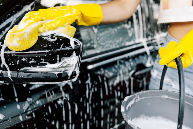 La mano di una donna con una spugna gialla per lavare, lavare un'auto.