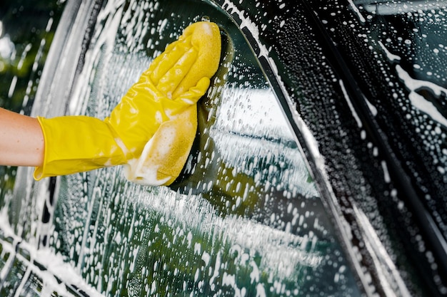 Foto la mano di una donna con una spugna gialla per lavare, lavare un'auto.