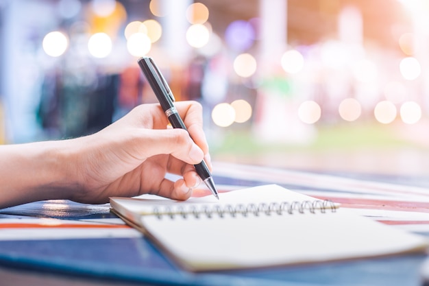 La mano della donna che scrive su un taccuino con una penna su una scrivania in legno.