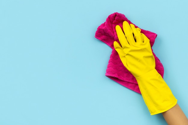 Woman's hand in yellow rubber glove wipe by rag blue background.