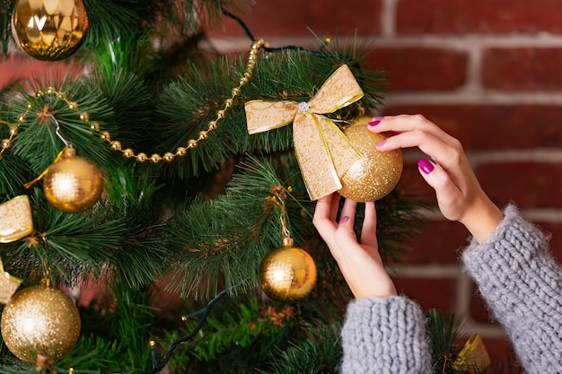 Woman's hands adorn Christmas tree by golden toy