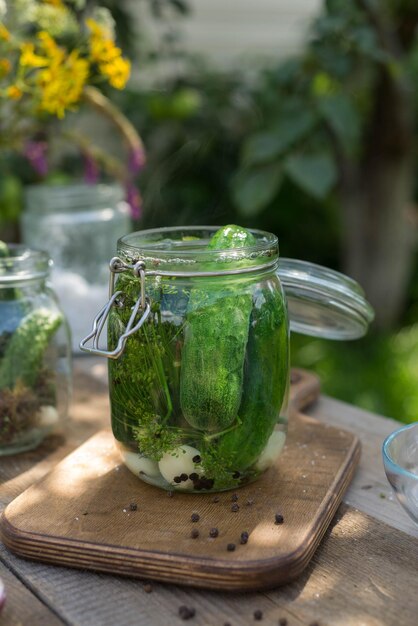 A woman's hands are pouring boiled water in a jar with pickled cucumbers