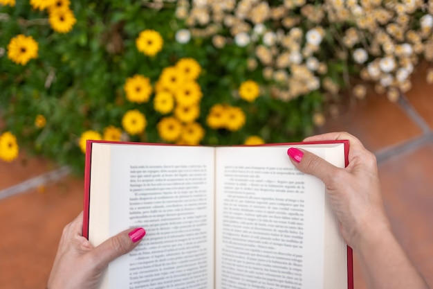 꽃 피는 식물 옆 정원에서 책을 읽는 동안 여자의 손에 책