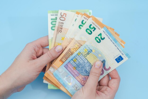 Woman's hands counting stack of euro banknotes on blue
background money business finance