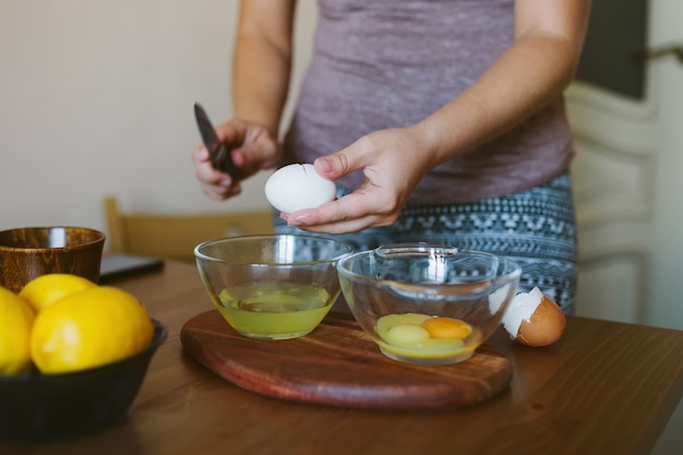 Руки женщины растрескивают целое яйцо в миску.