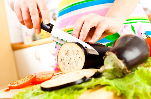 Woman's hands cutting aubergine eggplant , behind fresh vegetables.