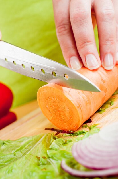 Woman's hands cutting carrot, behind fresh vegetables.