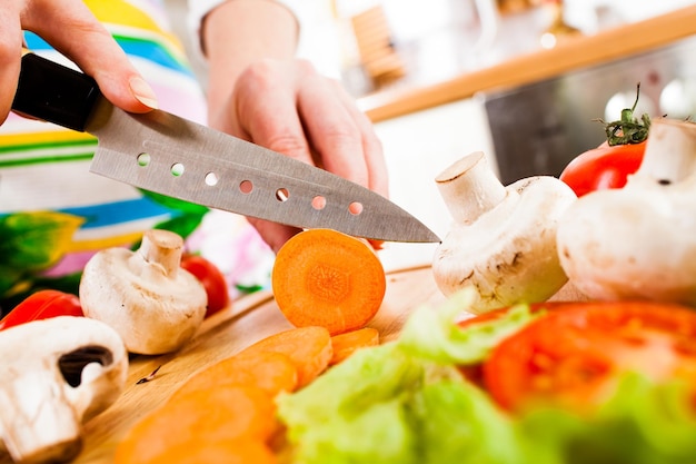 Woman's hands cutting carrot, behind fresh vegetables.