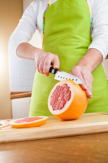 Woman's hands cutting fresh grapefruit on kitchen