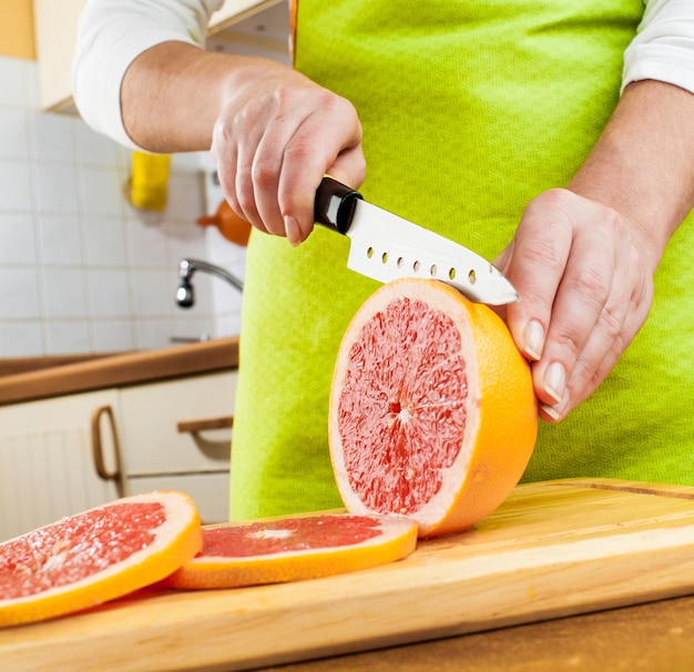 Photo woman's hands cutting fresh grapefruit on kitchen