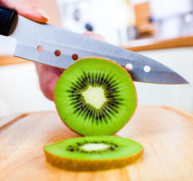 Photo woman's hands cutting fresh kiwi on kitchen