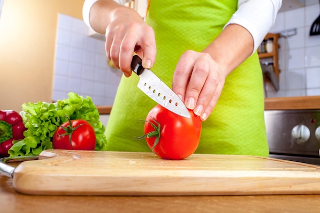 Woman's hands cutting fresh tomato on kitchen