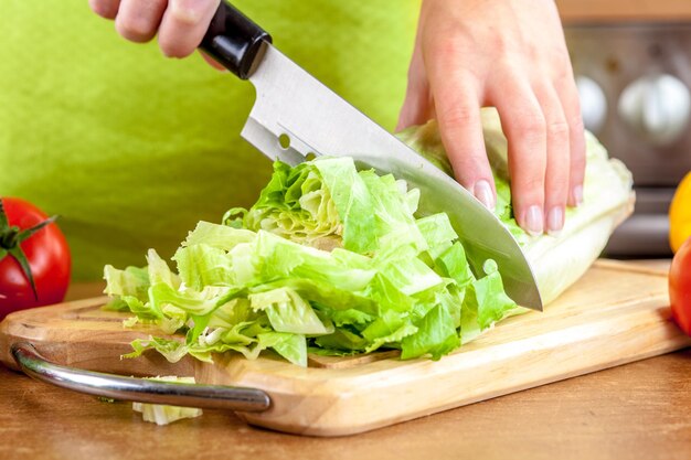 Woman's hands cutting lettuce, behind fresh vegetables.