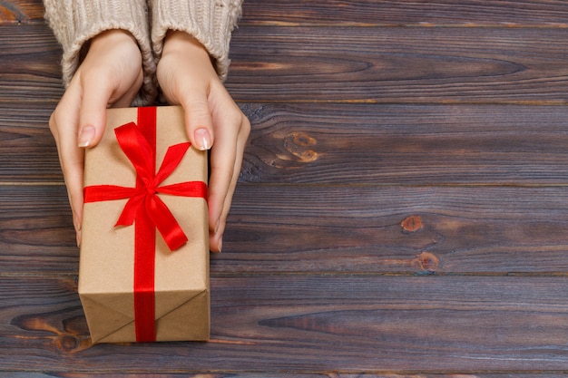 Woman's hands give wrapped valentine holiday handmade present in craft paper with red ribbon.