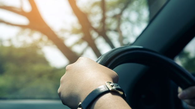 Woman's hands holding on black steering wheel while driving a car