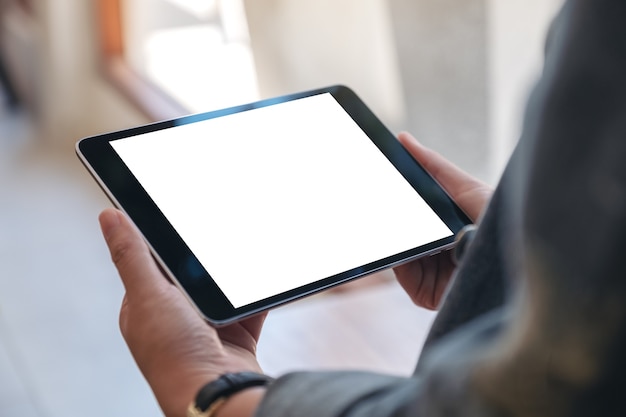 Foto mani della donna che tengono tablet pc nero con schermo vuoto orizzontalmente nella caffetteria