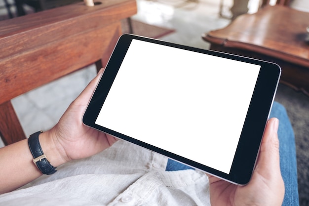 woman's hands holding black tablet pc with blank white screen horizontally while sitting in cafe