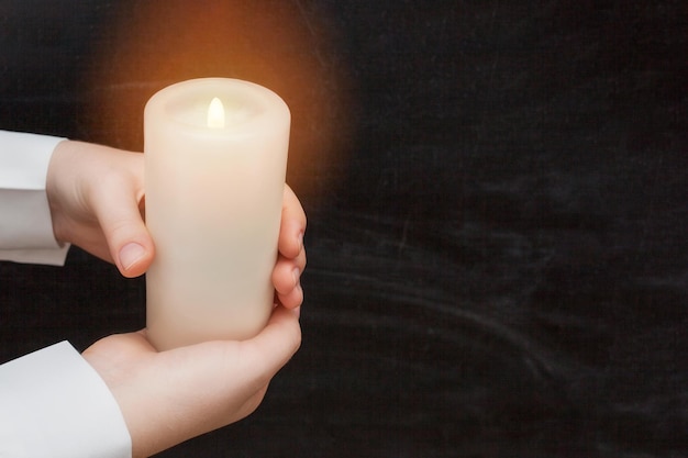 Woman's hands holding a burning candle on dark background. Close-up.