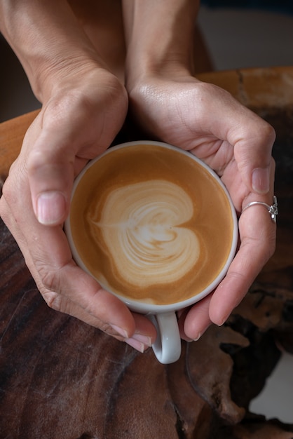 木製のテーブルにコーヒーのカップを保持している女性の手