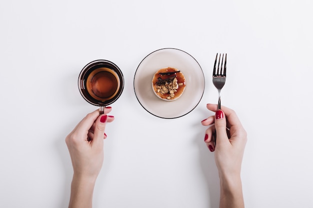 Foto le mani della donna che tengono una tazza di tè e un piatto con una torta