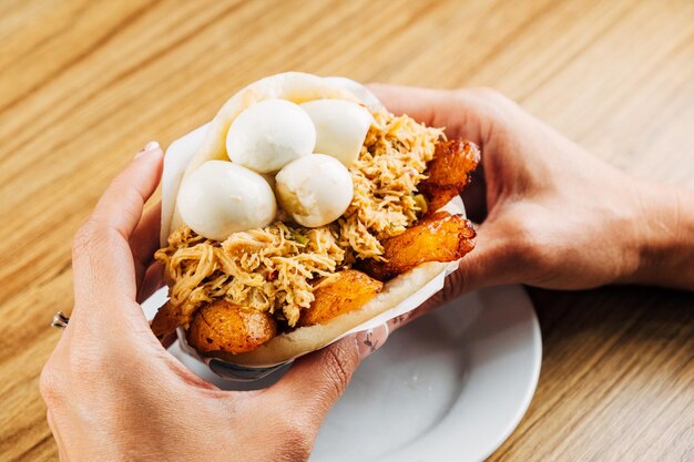 woman's hands holding delicious Venezuelan arepa stuffed with chicken fried plantain and corniz eggs