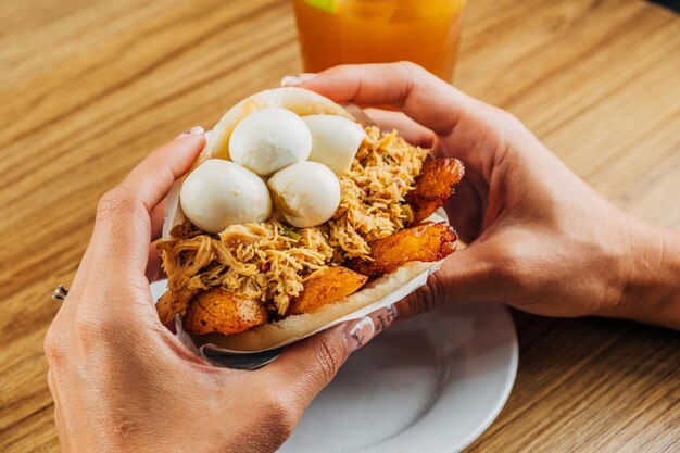 Photo woman's hands holding delicious venezuelan arepa stuffed with chicken fried plantain and corniz eggs