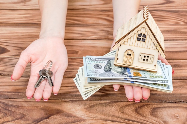 Woman's hands holding money model of house and keys of house in palms over wooden table