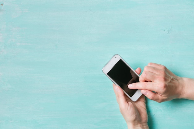 Woman's hands holding smartphone and typing on turquoise background