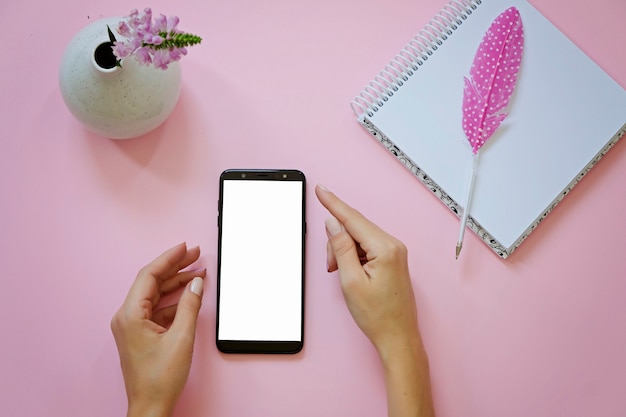 Le mani della donna che tengono smartphone con lo schermo in bianco, la penna con la piuma e il blocco note