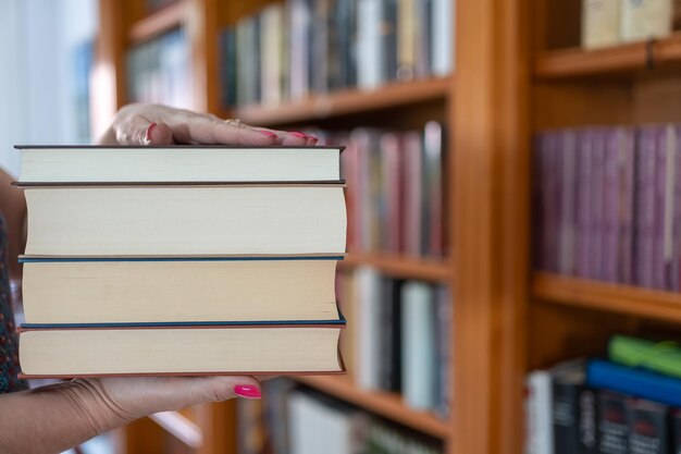 Woman's hands holding a stack of books in front of a bookstore full of books