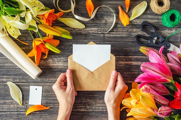 Woman's hands holds envelope with blank sheet and flowers decorations on wooden table