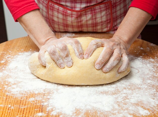 Woman's hands knead dough on wooden table