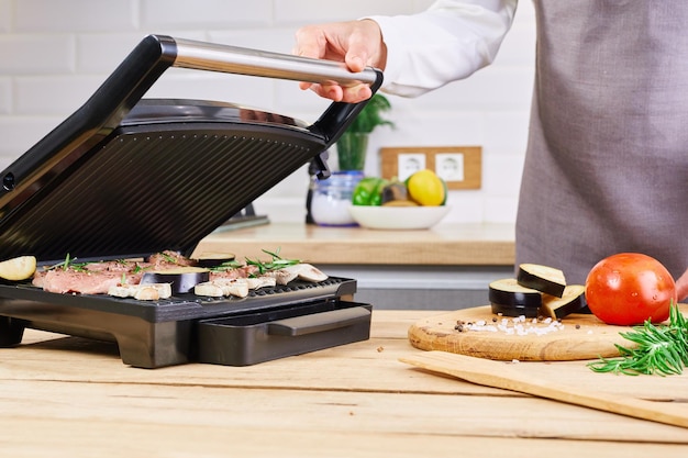 The woman\'s hands prepares meat on an electric grill on wooden\
table process of cooking meat on electric grill