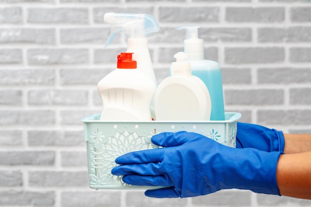 Woman's hands in protective gloves with bottles of glass cleaner in basket