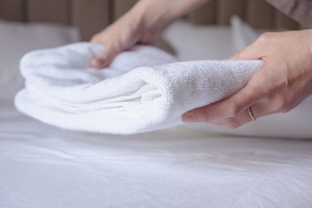 Woman's hands puts a clean white terry towel on the bed