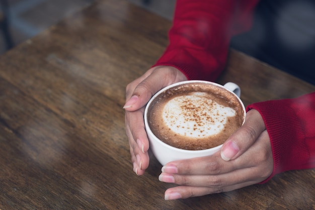 冬のカプチーノコーヒーのカップを保持している赤いキャディガンで女性の手。