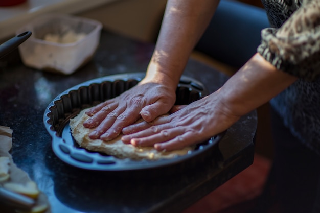 Mani di donna rotolare la pasta in teglia