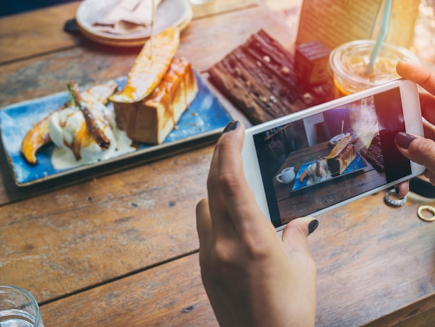 Woman's hands taking photo of the dessert on wooden table by smartphone