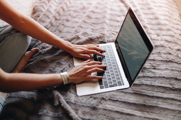 Foto le mani della donna che scrivono sulla tastiera del computer portatile nella camera da letto accogliente