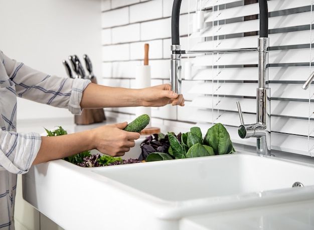 Photo woman's hands washing lettuce in kitchen sink close up.
