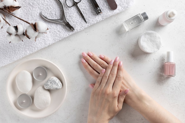 Woman's hands with delicate pink manicure on the wall of manicure tools. nails salon and spa. White concrete wall, top view.