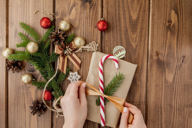 Руки женщины, упаковка Рождественский подарок, крупным планом. Неподготовленные рождественские подарки на деревянном с элементами декора и предметов, вид сверху. Рождество или Новый год DIY упаковка.