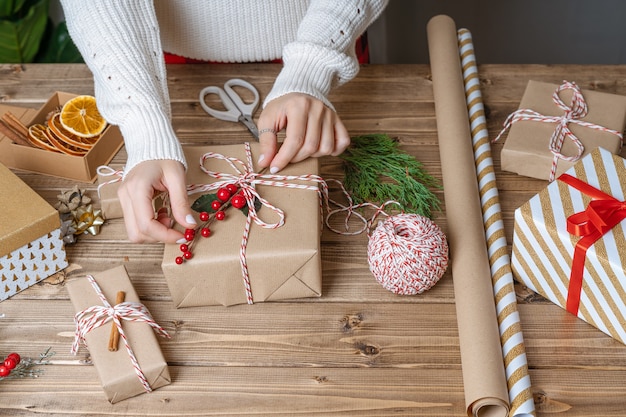 Le mani della donna che avvolgono il regalo di natale si chiudono su regali impreparati su sfondo di legno con decorazioni