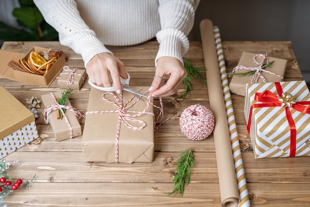 Le mani della donna che avvolgono il regalo di natale si chiudono su regali impreparati su sfondo di legno con decorazioni