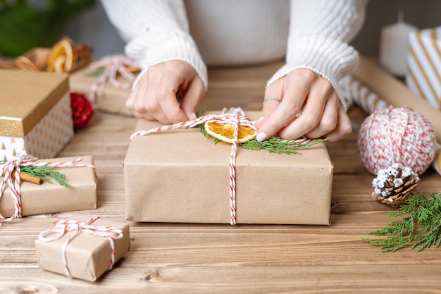 Woman s hands wrapping christmas gift close up unprepared presents on wooden background with decor