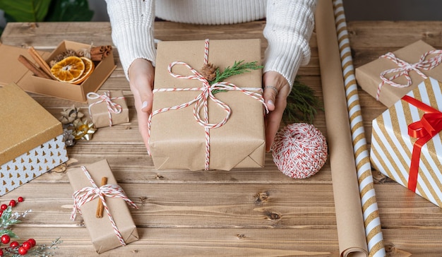 Le mani della donna che avvolgono il regalo di natale si chiudono su regali impreparati su sfondo di legno con decorazioni