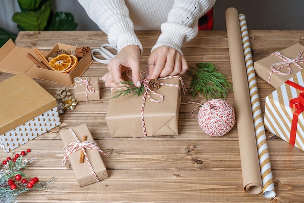 Woman s hands wrapping christmas gift close up unprepared presents on wooden background with decor