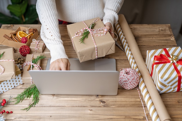 Woman s hands wrapping Christmas gift and using laptop