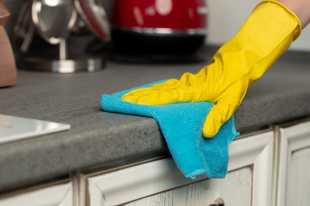 Woman's hands in yellow gloves cleaning counter top in kitchen