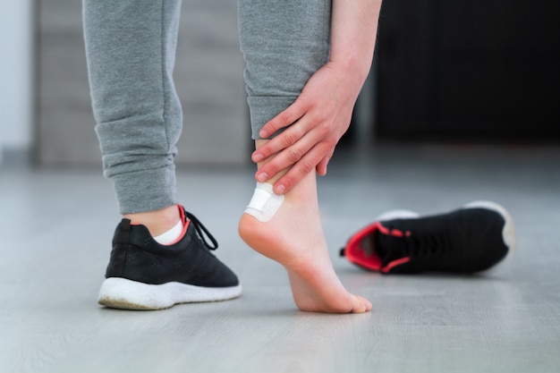 Woman's heel with white medical adhesive plaster from calluses during wearing a new shoe. Skin care feet and prevention of calluses and corns